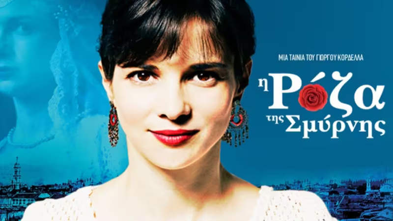 A woman with dark hair and radiant skin smiles confidently, wearing vibrant earrings and lipstick. In the background, a ghostly silhouette and a blue-toned cityscape can be seen, along with stylized text that reads "η Ρόζα της Σμύρνης," suggesting a film title.